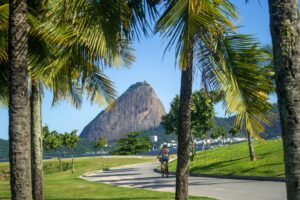 A cyclist rides through a park with a view of the iconic Sugarloaf Mountain in Rio de Janeiro.