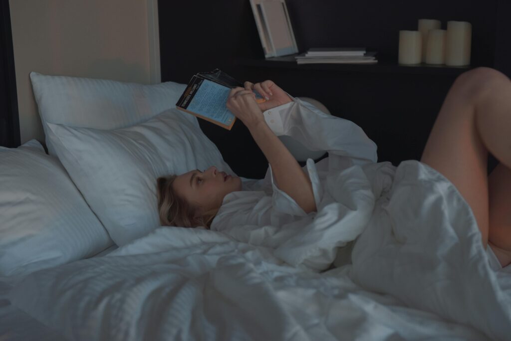 A woman comfortably reading a book in a cozy bedroom setting.