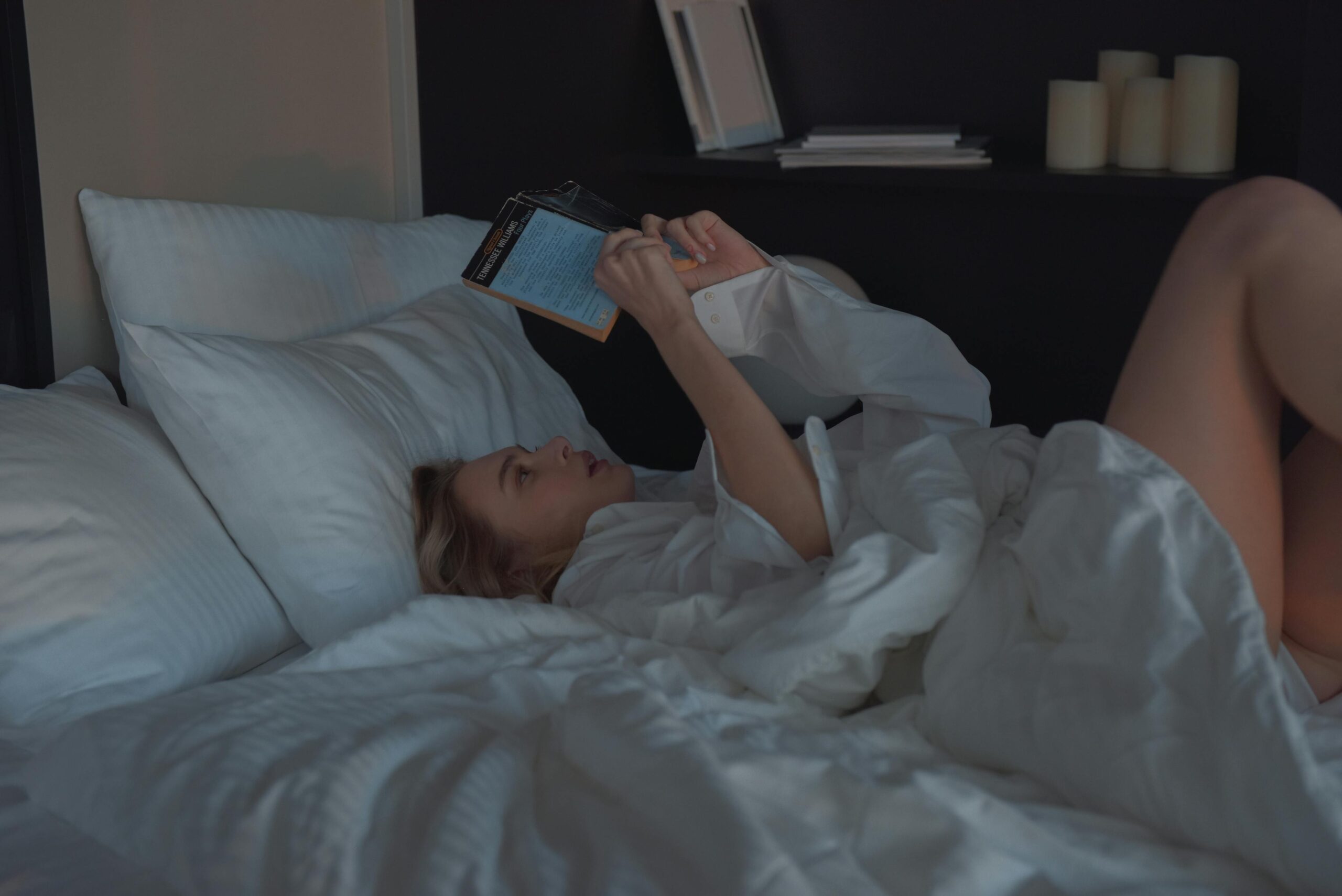 A woman comfortably reading a book in a cozy bedroom setting.